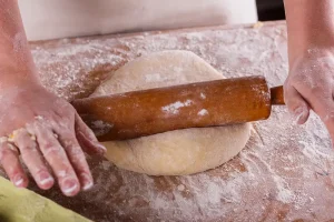 young-woman-in-apron-kneading-food-Nanny-Pizza-dough-on-board